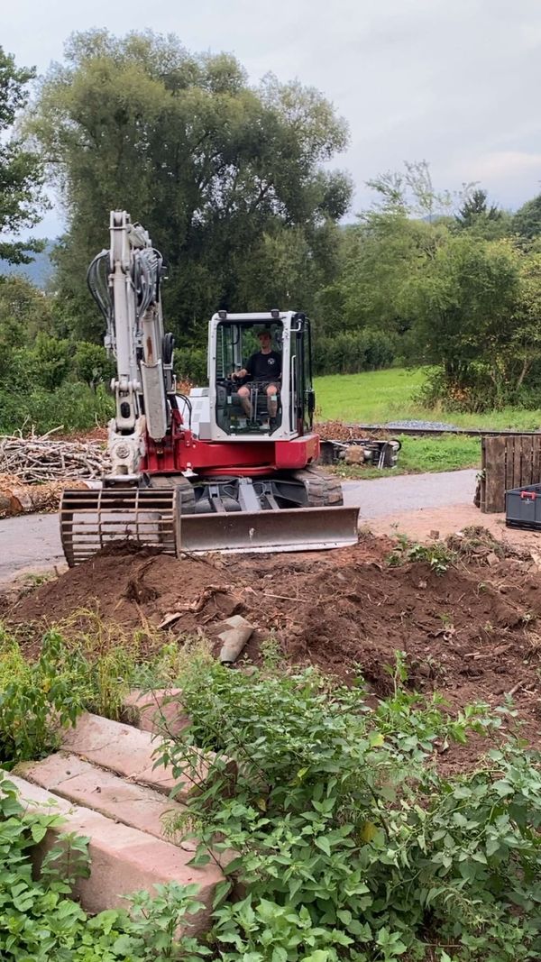 Bagger schiebt Erdreich am Hang zurecht und modelliert das Gelände neben einer Sandsteintreppe
