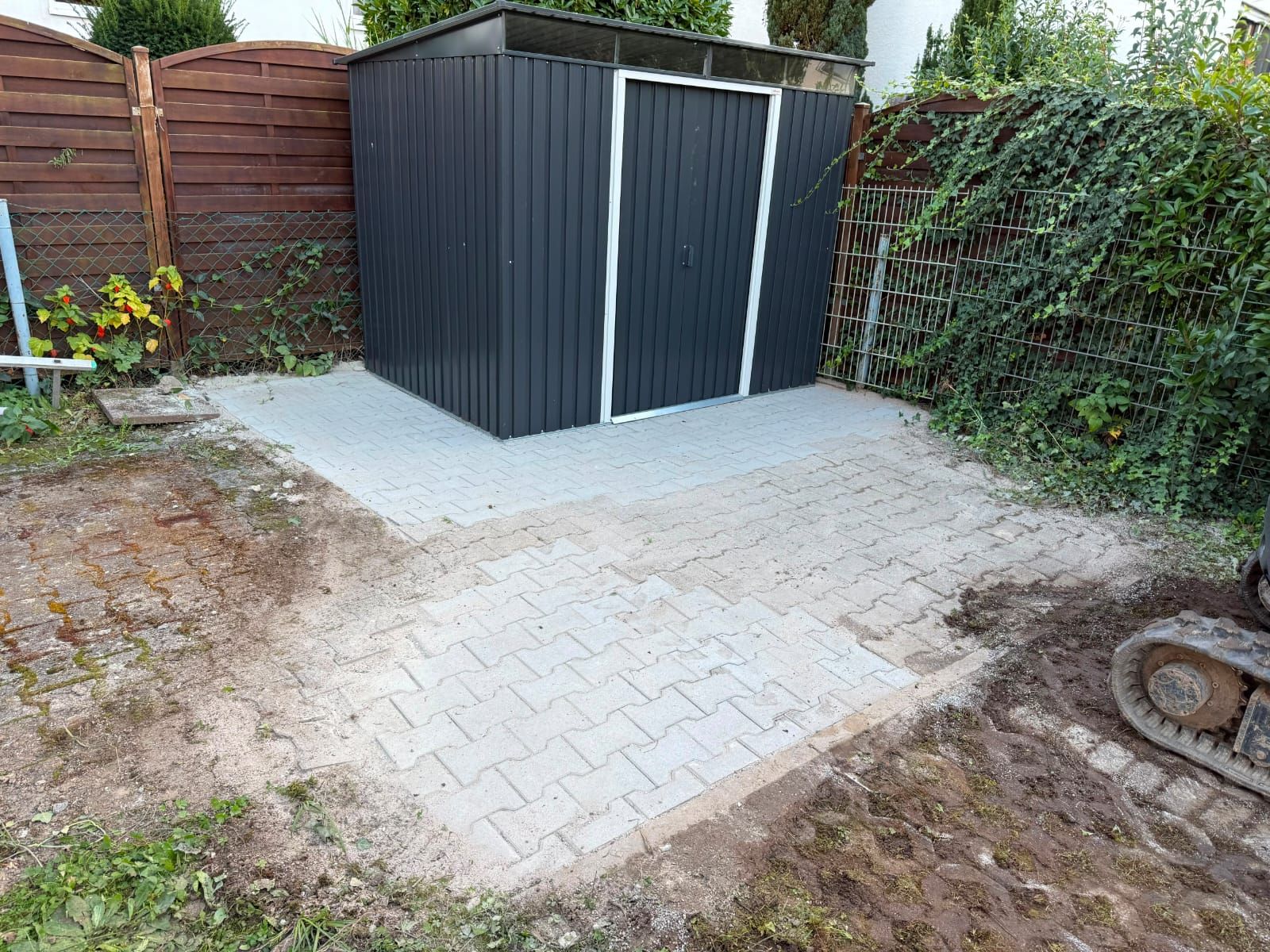 Neu gepflasterte Standfläche mit aufgestelltem Gerätehaus in einem Hausgarten