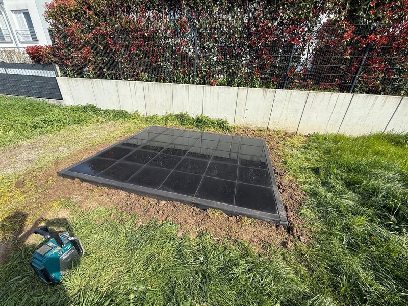 Fertig verlegte Plattenfläche in Anthrazit mit gesetzter Randeinfassung, angelegt als ebene Standfläche im Garten vor Mauer und Hecke